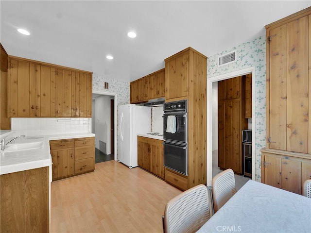 kitchen featuring wallpapered walls, a sink, light countertops, under cabinet range hood, and light wood-type flooring