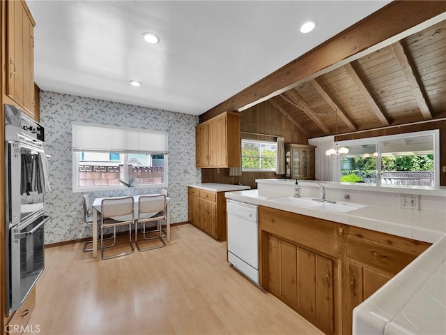kitchen featuring white dishwasher, a sink, double oven, wallpapered walls, and light wood-type flooring