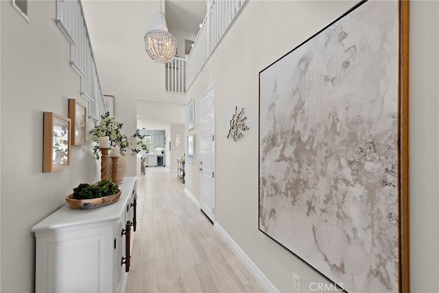 hallway featuring a towering ceiling, visible vents, an inviting chandelier, light wood finished floors, and baseboards