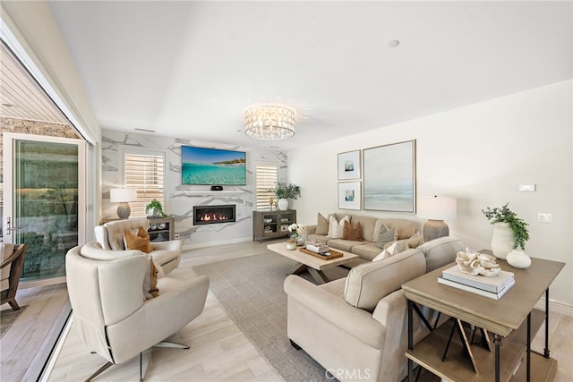 living room with light wood finished floors, a chandelier, baseboards, and a high end fireplace