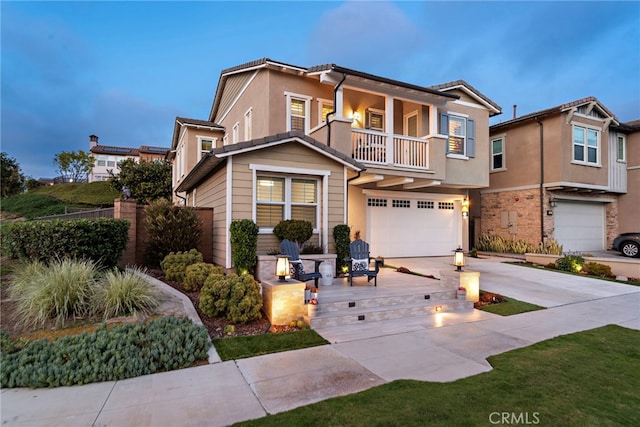 traditional home featuring a balcony, driveway, stucco siding, and an attached garage