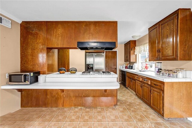 1414 Fairplain Ave, Whittier, CA 90601 - kitchen with a peninsula, stainless steel appliances, exhaust hood, brown cabinets, and visible vents