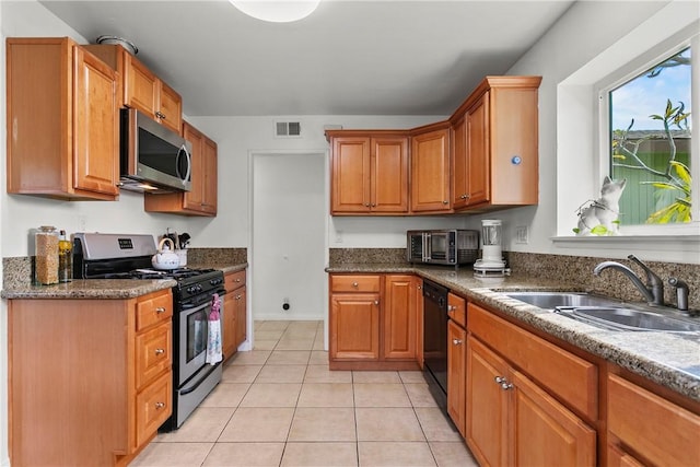 kitchen with brown cabinetry, visible vents, appliances with stainless steel finishes, a sink, and light tile patterned floors