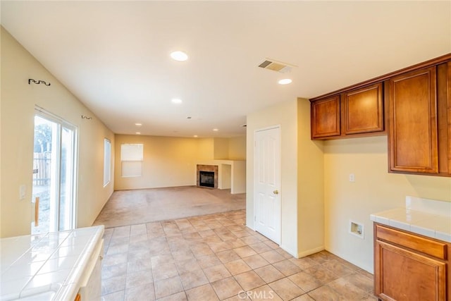 14051 Mare Ln, Victorville, CA 92394 - kitchen featuring tile countertops, brown cabinets, light carpet, a glass covered fireplace, and recessed lighting