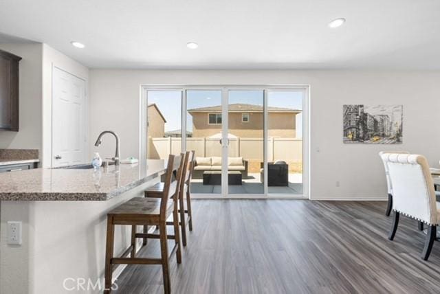 3308 Jack Rabbit Ct, Perris, CA 92570 - kitchen with light stone counters, a sink, a kitchen island with sink, a kitchen bar, and dark wood-style flooring