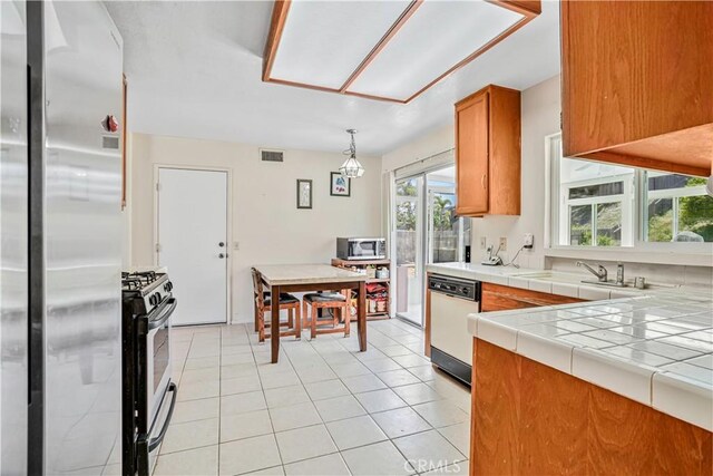 1426 Crestview Dr, Oceanside, CA 92056 - kitchen featuring stainless steel appliances, brown cabinets, tile counters, light tile patterned floors, and decorative light fixtures