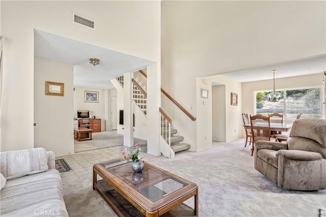 living room featuring visible vents, a high ceiling, stairway, light colored carpet, and a notable chandelier