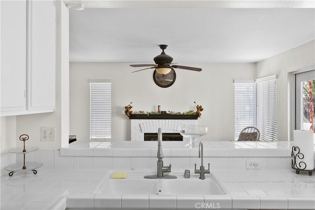 kitchen with white cabinets, tile countertops, ceiling fan, and a sink
