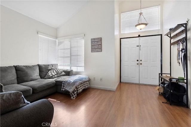 living area with baseboards, light wood-type flooring, and high vaulted ceiling