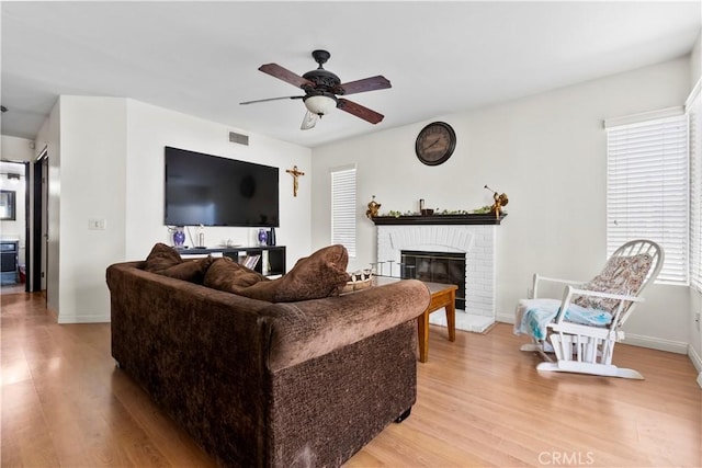 living area featuring a ceiling fan, a brick fireplace, light wood-style floors, and a healthy amount of sunlight