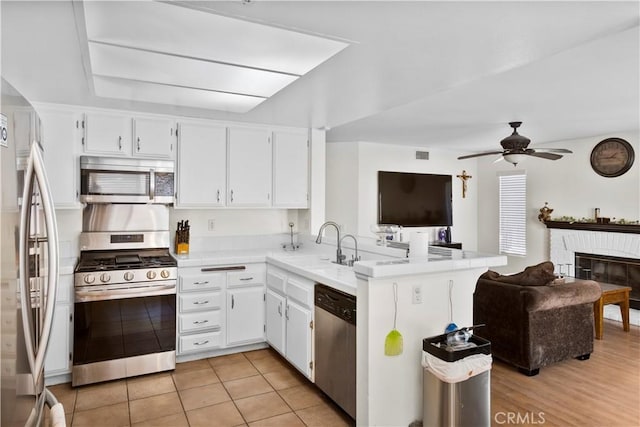 kitchen featuring light countertops, a sink, a peninsula, appliances with stainless steel finishes, and open floor plan