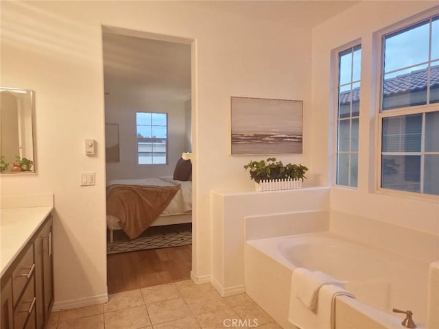 ensuite bathroom with connected bathroom, tile patterned flooring, vanity, baseboards, and a garden tub