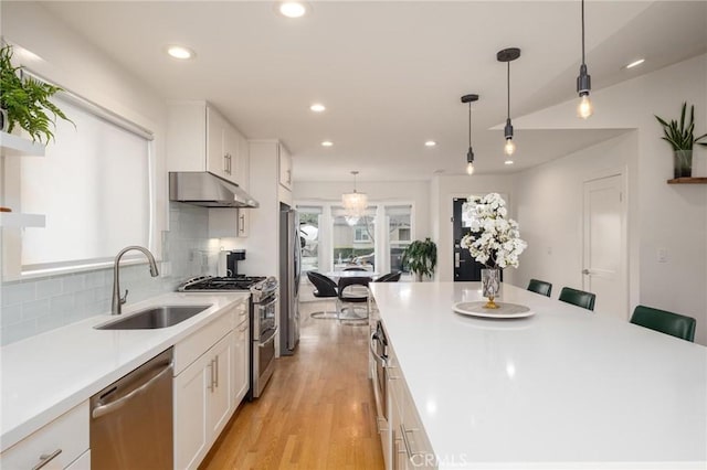 kitchen featuring white cabinets, a sink, recessed lighting, under cabinet range hood, and appliances with stainless steel finishes