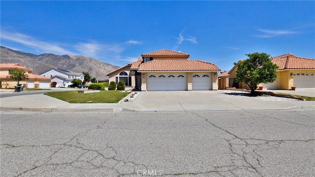 view of front facade with a tiled roof, a mountain view, concrete driveway, a garage, and stucco siding