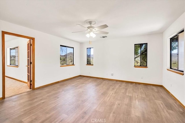 empty room featuring visible vents, light wood finished floors, ceiling fan, and a healthy amount of sunlight