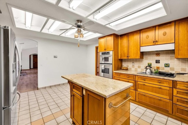 kitchen with arched walkways, under cabinet range hood, light tile patterned flooring, and stainless steel appliances