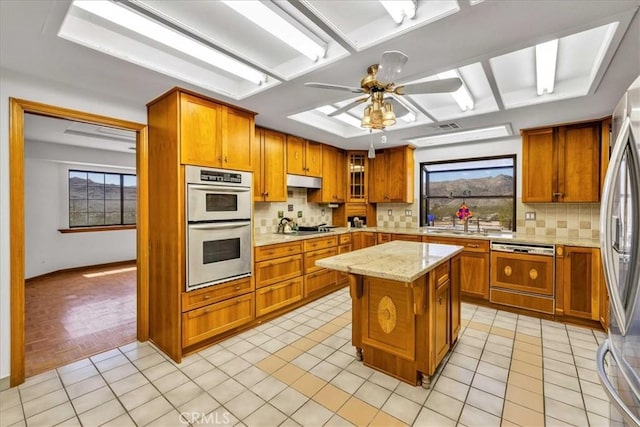 kitchen featuring decorative backsplash, ceiling fan, brown cabinetry, and stainless steel appliances