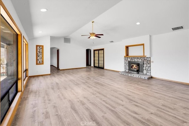 unfurnished living room featuring a fireplace, arched walkways, wood finished floors, lofted ceiling, and visible vents