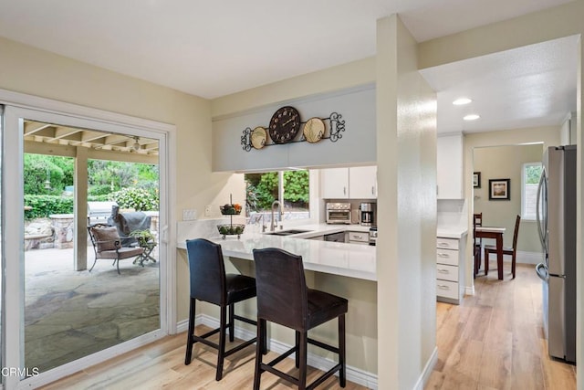 kitchen featuring freestanding refrigerator, a wealth of natural light, white cabinets, a sink, and a peninsula