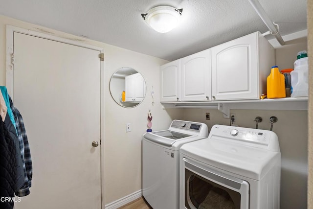 clothes washing area featuring baseboards, cabinet space, a textured ceiling, and washing machine and clothes dryer
