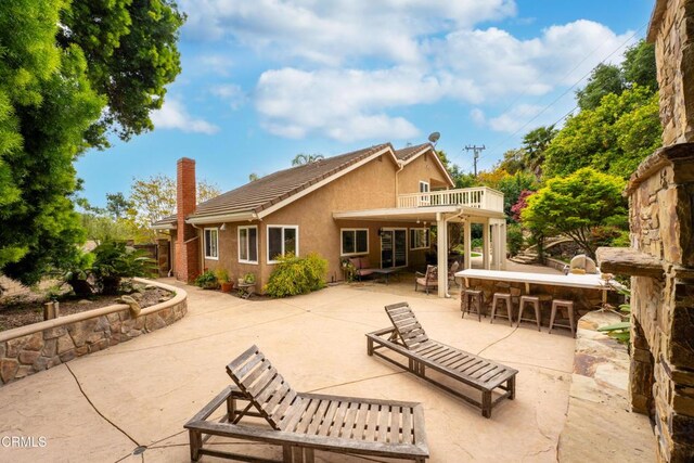 rear view of property with stucco siding, a chimney, outdoor dry bar, and a patio