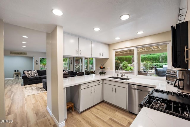 kitchen featuring white cabinetry, stainless steel dishwasher, a sink, light wood-type flooring, and recessed lighting
