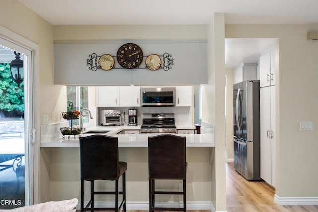 kitchen featuring stainless steel appliances, light countertops, white cabinets, a sink, and a peninsula