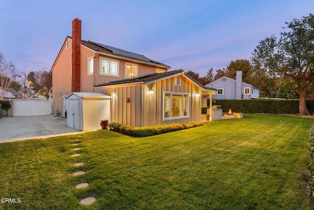 1894 Rambling Rd, Simi Valley, CA 93065 - back of house at dusk featuring roof mounted solar panels, a chimney, a patio, a storage shed, and board and batten siding