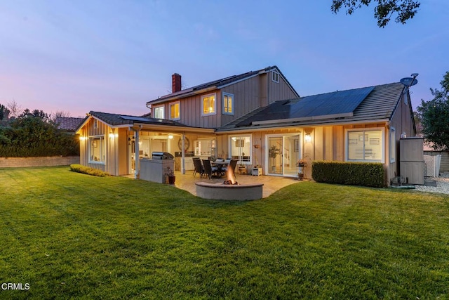 1894 Rambling Rd, Simi Valley, CA 93065 - back of house at dusk with board and batten siding, a chimney, a yard, roof mounted solar panels, and area for grilling