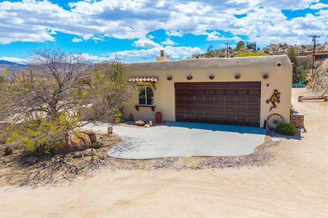 57710 Bandera Rd, Yucca Valley, CA 92284 - pueblo revival-style home featuring a garage, stucco siding, a chimney, and driveway