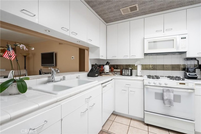 kitchen with visible vents, light tile patterned flooring, white appliances, white cabinetry, and a sink