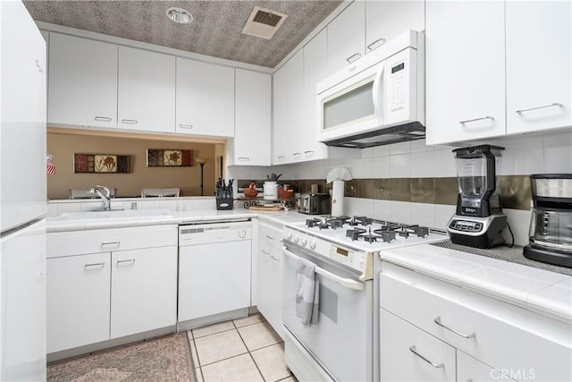 kitchen featuring tile countertops, visible vents, a sink, white appliances, and white cabinetry