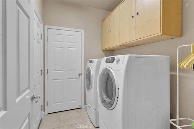 clothes washing area featuring washing machine and clothes dryer, light tile patterned flooring, and cabinet space