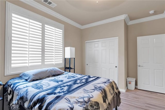 bedroom with ornamental molding, light wood finished floors, visible vents, and a closet