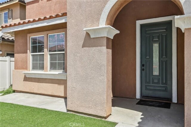 doorway to property featuring fence and stucco siding