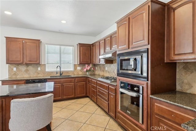 kitchen featuring under cabinet range hood, dark stone countertops, backsplash, a sink, and appliances with stainless steel finishes