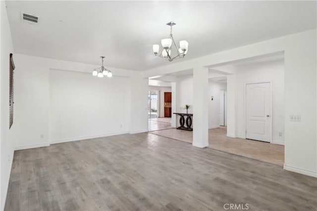 unfurnished living room featuring wood finished floors, visible vents, baseboards, and an inviting chandelier