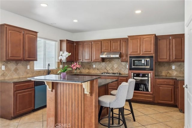 kitchen featuring light tile patterned flooring, under cabinet range hood, a breakfast bar area, and stainless steel appliances