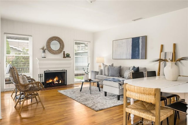 living room featuring a fireplace with flush hearth, light wood-style flooring, and visible vents