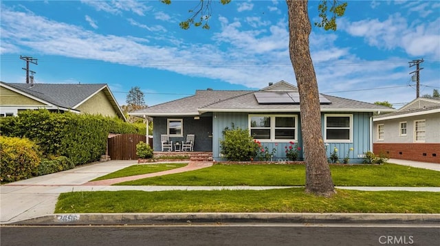 bungalow-style home with a front lawn, covered porch, fence, board and batten siding, and roof mounted solar panels