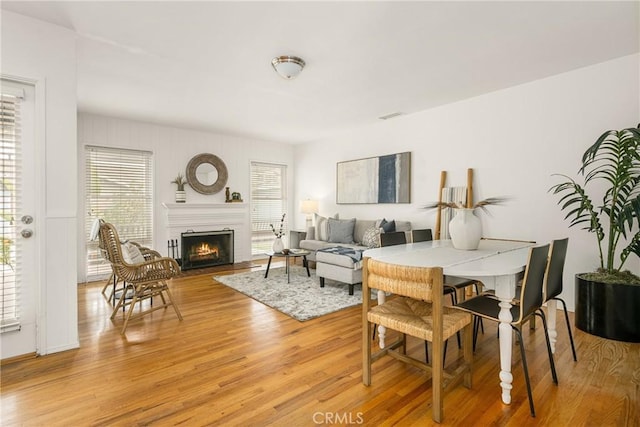 dining room featuring light wood-style floors, visible vents, and a lit fireplace