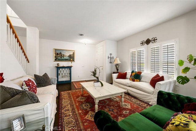 living area with baseboards, wood finished floors, visible vents, and stairway