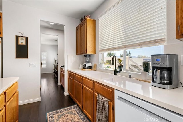 kitchen featuring light countertops, a sink, white dishwasher, baseboards, and dark wood-style flooring