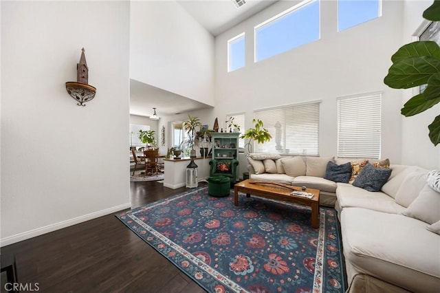 living room featuring visible vents, a towering ceiling, baseboards, and wood finished floors
