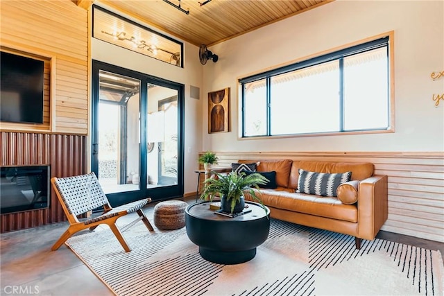 living area featuring healthy amount of natural light, wood walls, and concrete flooring