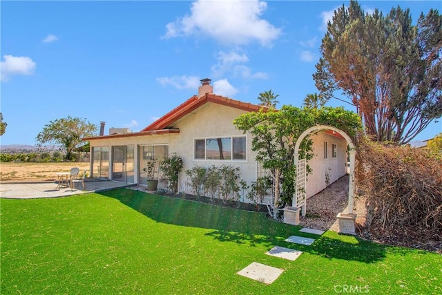 back of house with a lawn, a patio, a chimney, and stucco siding