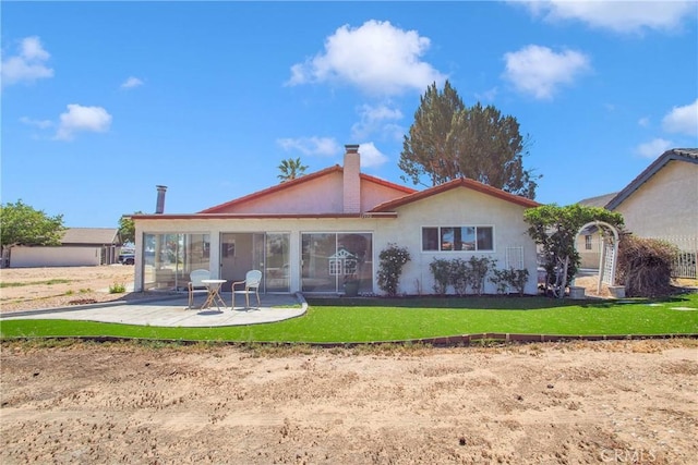 back of house with a patio area, stucco siding, a yard, and a chimney