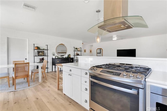 kitchen with white cabinets, stainless steel gas range oven, light wood-style floors, light countertops, and visible vents
