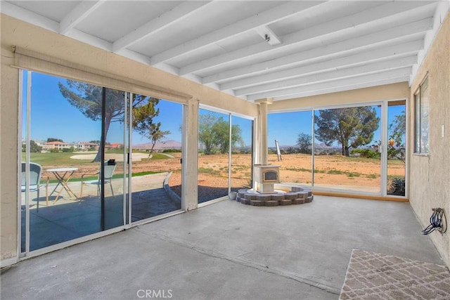unfurnished sunroom featuring a wood stove, a healthy amount of sunlight, beam ceiling, and unfinished concrete floors