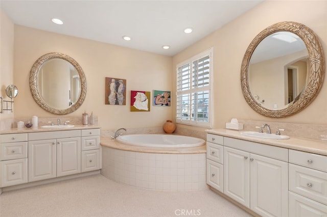 bathroom with two vanities, recessed lighting, a bath, and a sink
